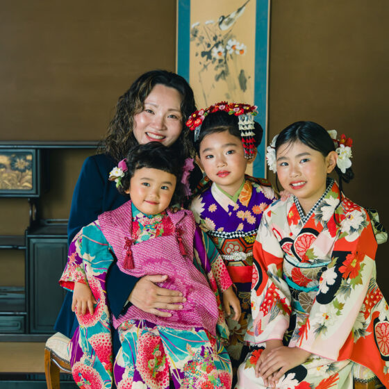 七五三用アンティーク着物姿の三姉妹と母親が和室で笑顔で撮影する家族写真シーン